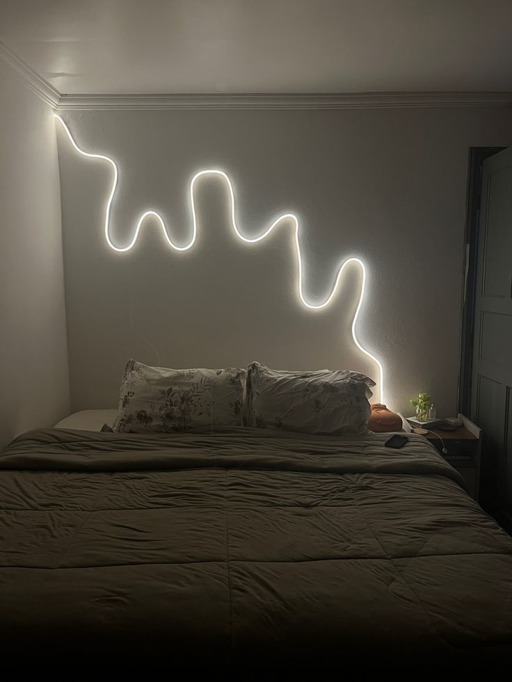 a bed that has some lights on the headboard and pillows in front of it