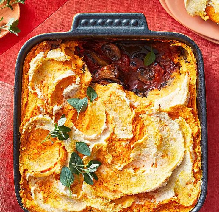 a casserole dish with eggs, meat and vegetables in it on a red table cloth