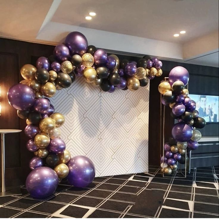 a purple and gold balloon arch in the middle of a room with black tile flooring