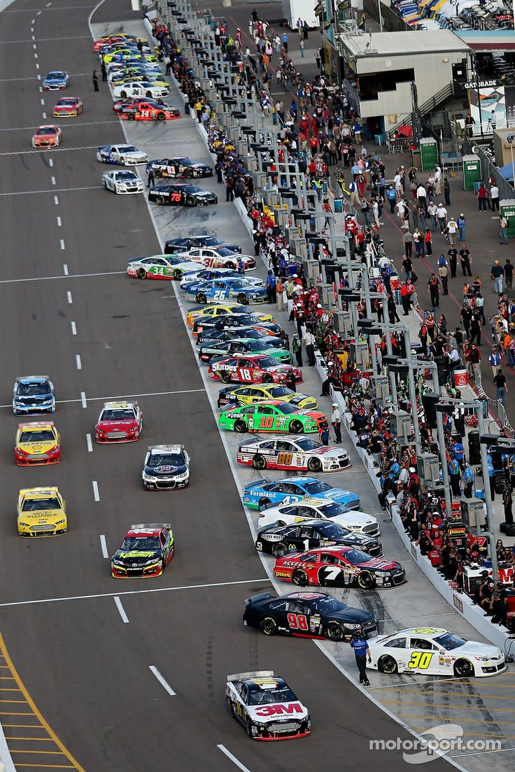 a group of cars driving down a race track with people standing on the sidelines