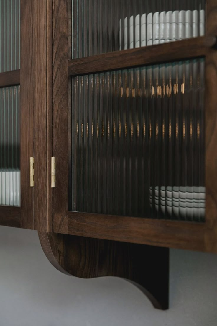 a wooden cabinet with glass doors and plates on it's sides, in front of a white wall