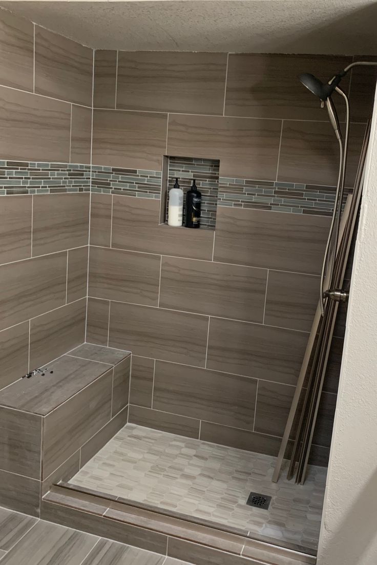 a walk in shower sitting next to a tiled wall and wooden floored area with gray tiles on the walls