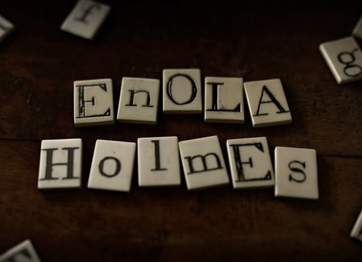 the word enola homes spelled with small tiles on a wooden table in black and white