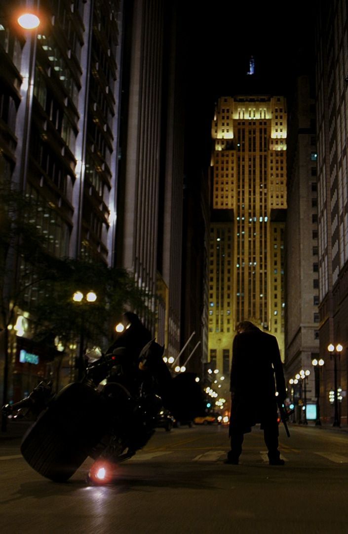 a man standing in the middle of a city at night with his motorcycle parked on the street