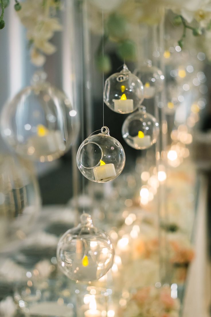 some clear glass balls hanging from the ceiling with flowers in them and candles on the table