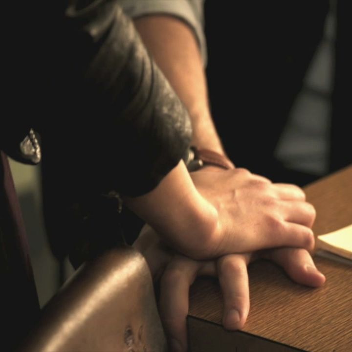 two people sitting at a table with their hands resting on each other's arm