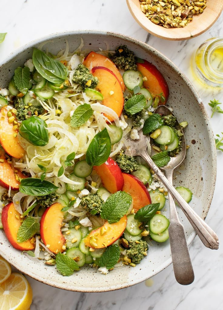 a bowl filled with vegetables and fruit next to sliced lemons on a white table