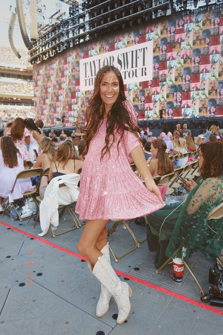 a woman in a pink dress and cowboy boots posing for the camera at a concert