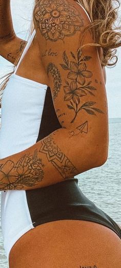 a woman with tattoos on her body standing in front of the ocean