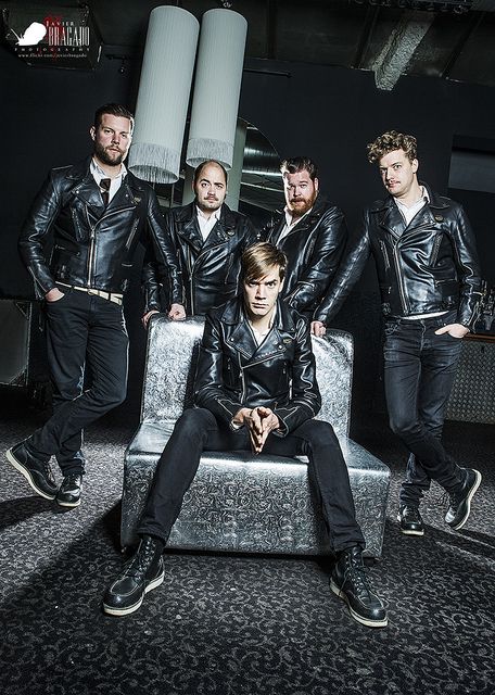 a group of men sitting on top of a silver couch in front of a wall