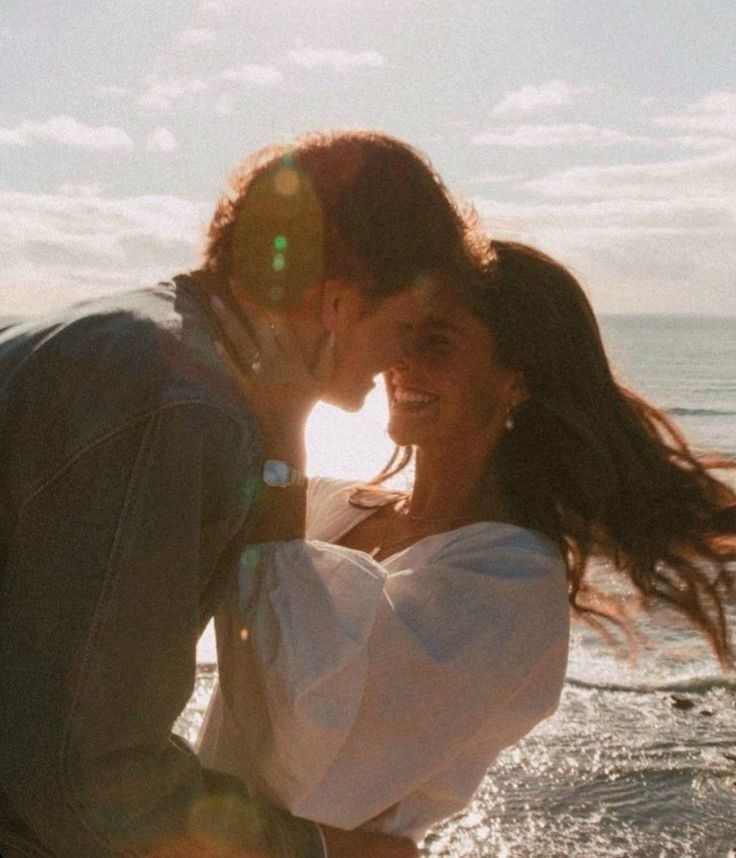 a man and woman kissing on the beach with sun flares in the sky behind them