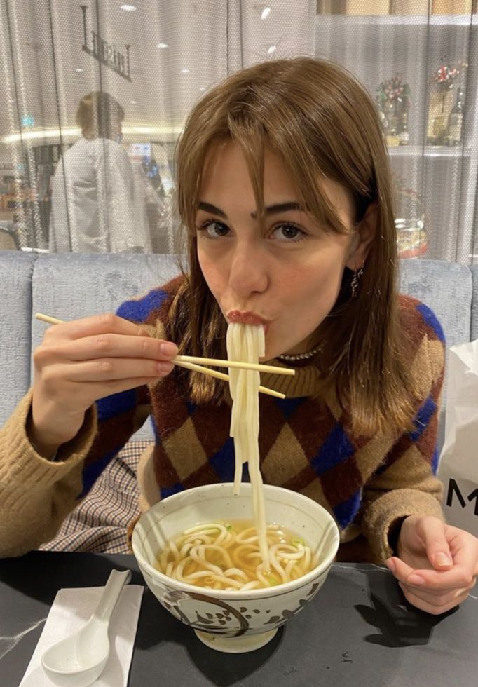 a woman sitting at a table eating noodles