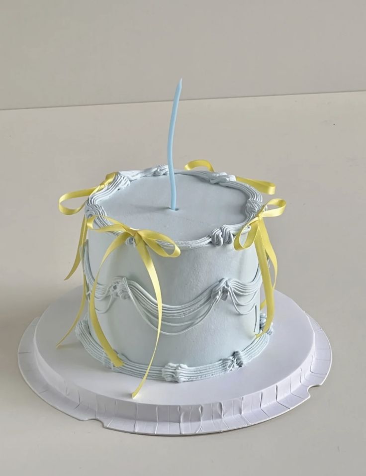 a white cake with yellow ribbons and a single candle