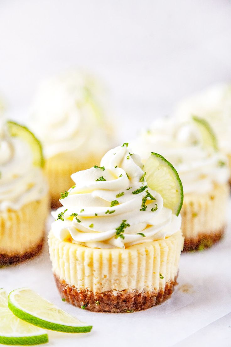 several small cupcakes with lime slices and whipped cream on top, sitting next to each other