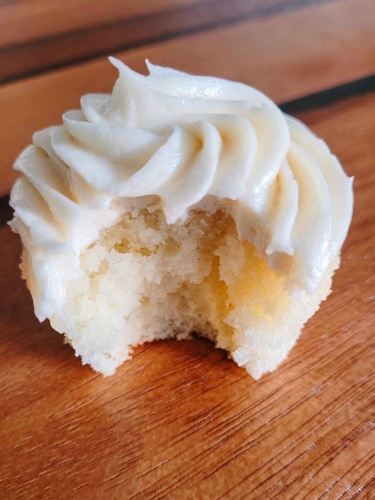 a half eaten cupcake with white frosting on a wooden table