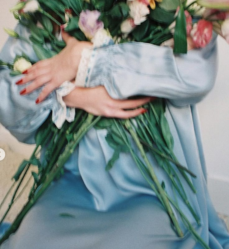 a woman in a blue dress holding a bouquet of flowers with her hands on her chest