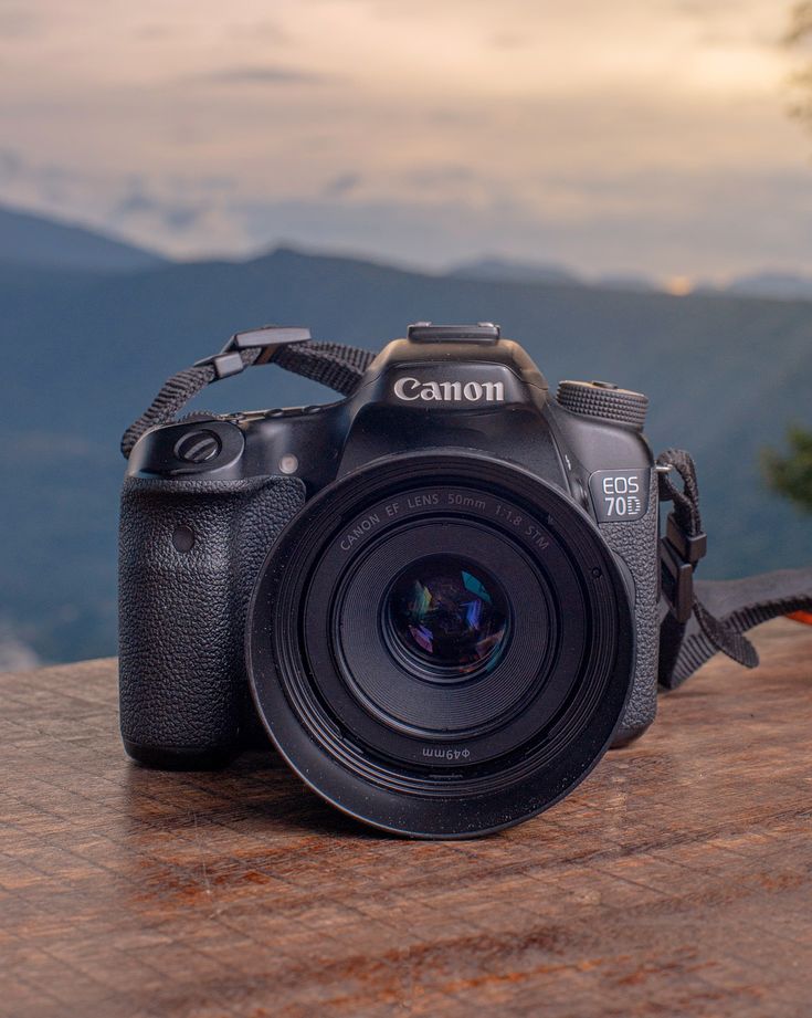 a camera sitting on top of a wooden table with mountains in the backgroud