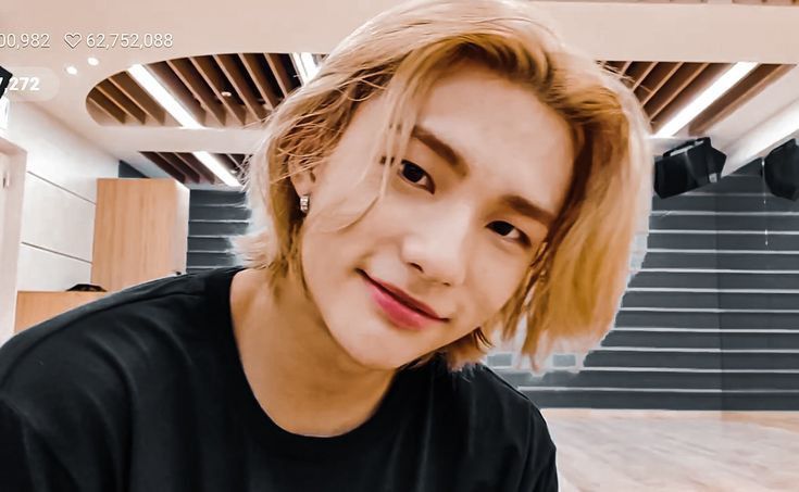 a young man with blonde hair and black shirt sitting in front of stairs looking at the camera