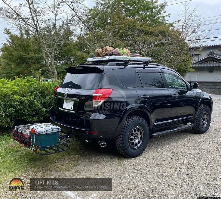 a black suv parked in front of a house with luggage strapped to the roof rack