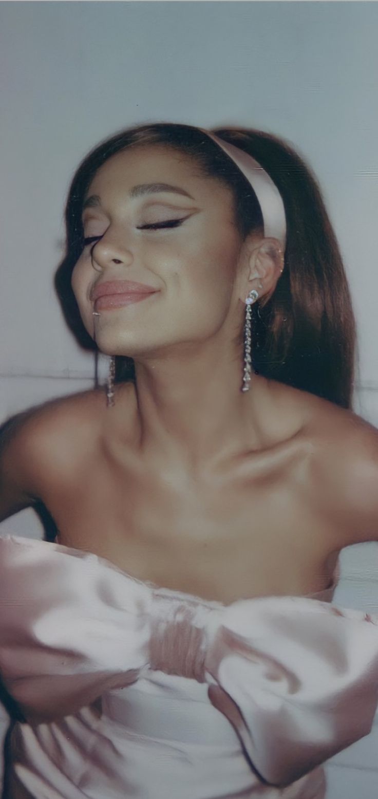 a woman in a white dress with her eyes closed and wearing large earrings on her head