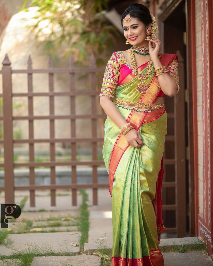 a woman in a green and red sari posing for the camera with her hand on her hip