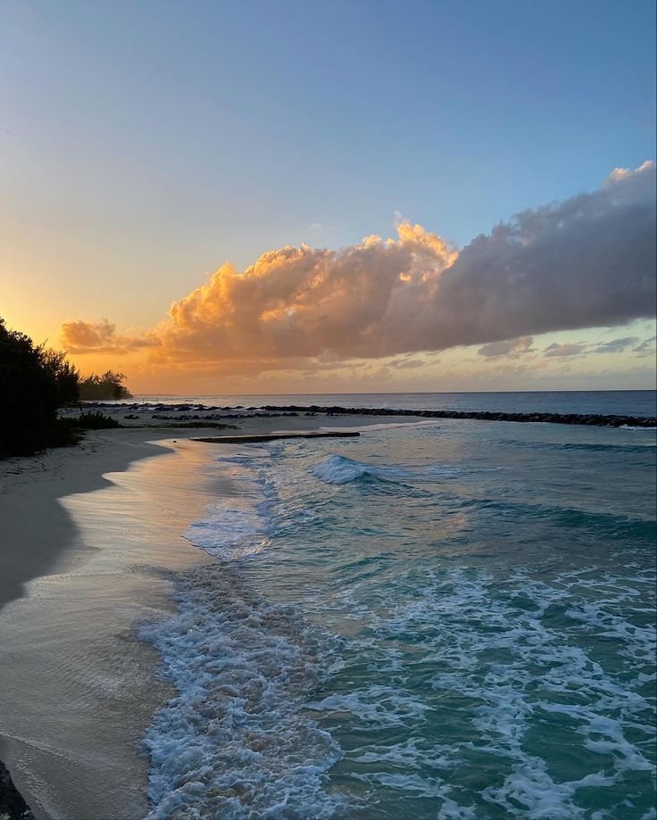 the sun is setting over the ocean with waves coming in