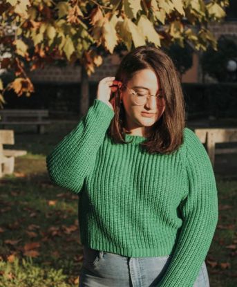 a woman standing in front of a tree wearing a green sweater