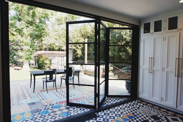 an open glass door leading to a patio area with black and white tiles on the floor