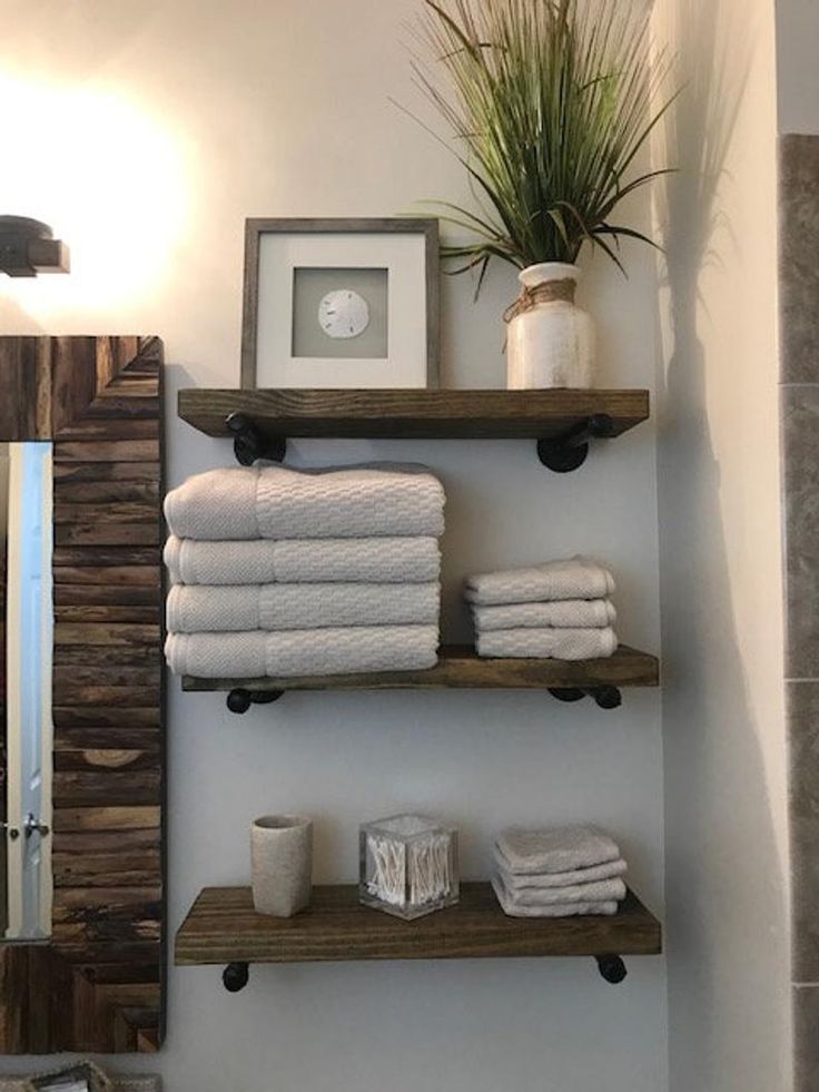 a bathroom with shelves and towels on the wall next to a mirror, toilet paper rolls and a potted plant