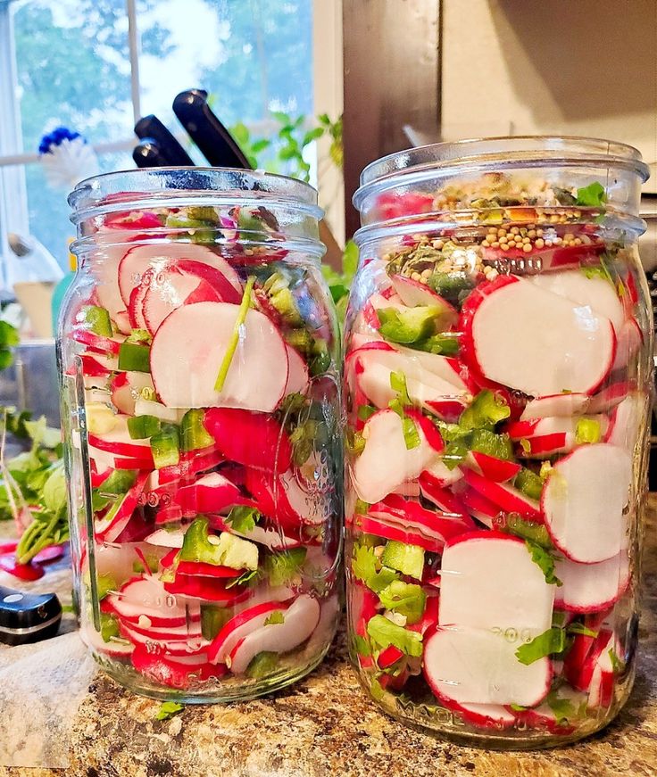 two mason jars filled with sliced radishes and other veggies on a kitchen counter