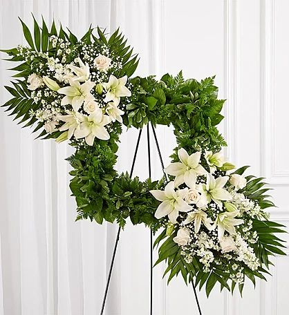 two wreaths with white flowers and greenery on them in front of a white wall