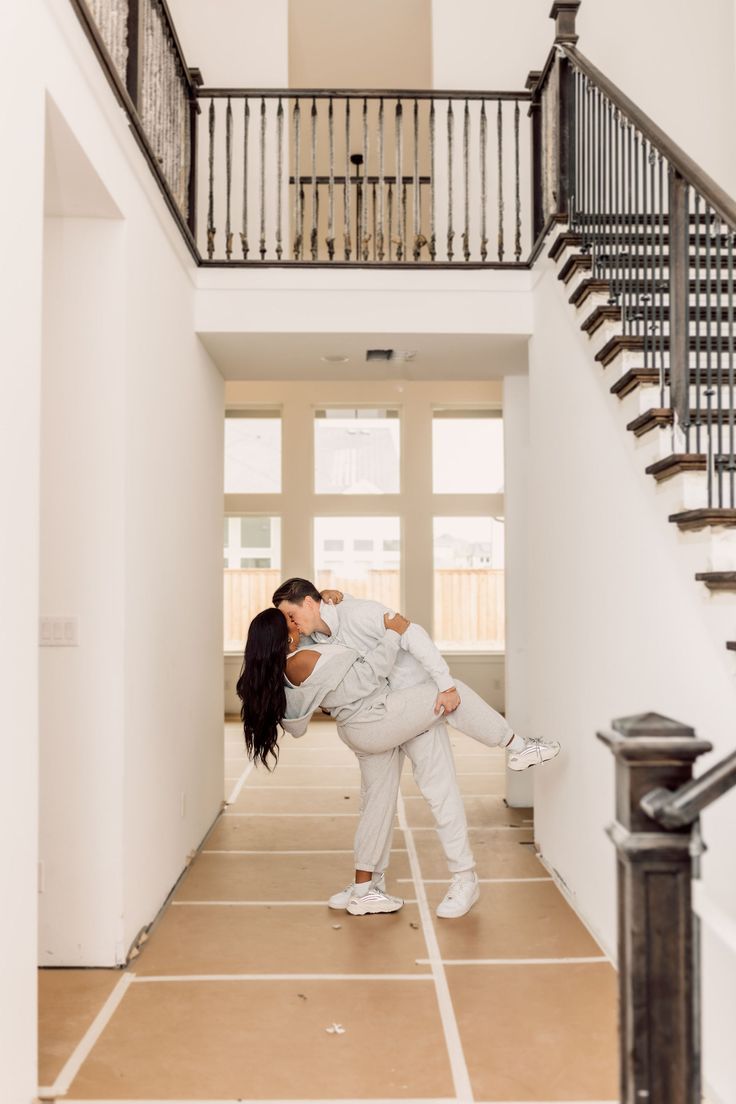 a couple kissing in the middle of a hallway with stairs and balconies on either side