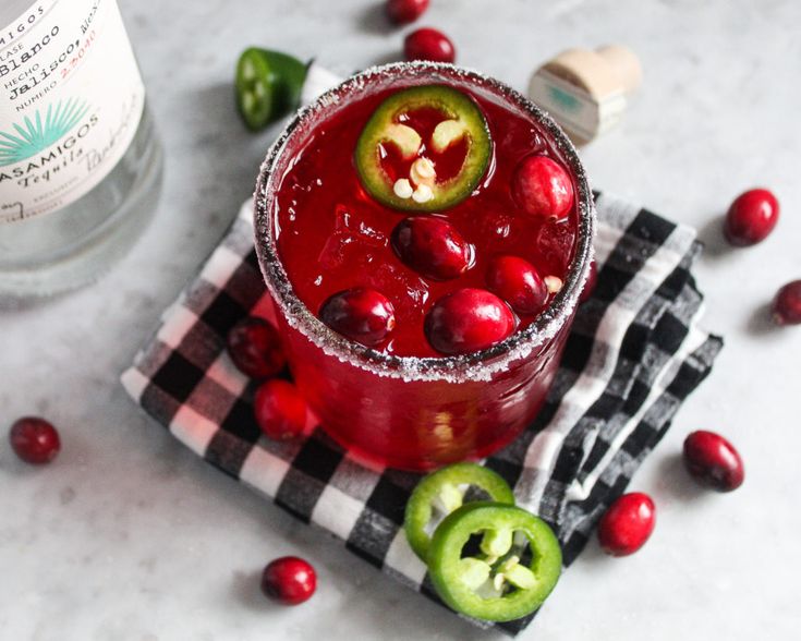 a red drink with cranberry and jalapenos on the table next to it