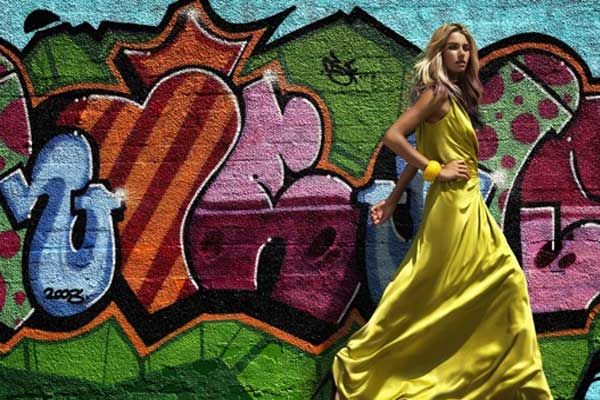 a woman in a long yellow dress walking by graffiti