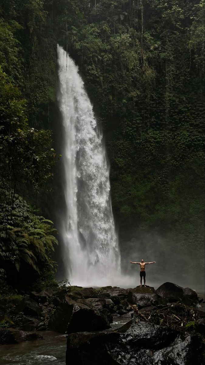 a man standing in front of a waterfall with his arms spread out to the side