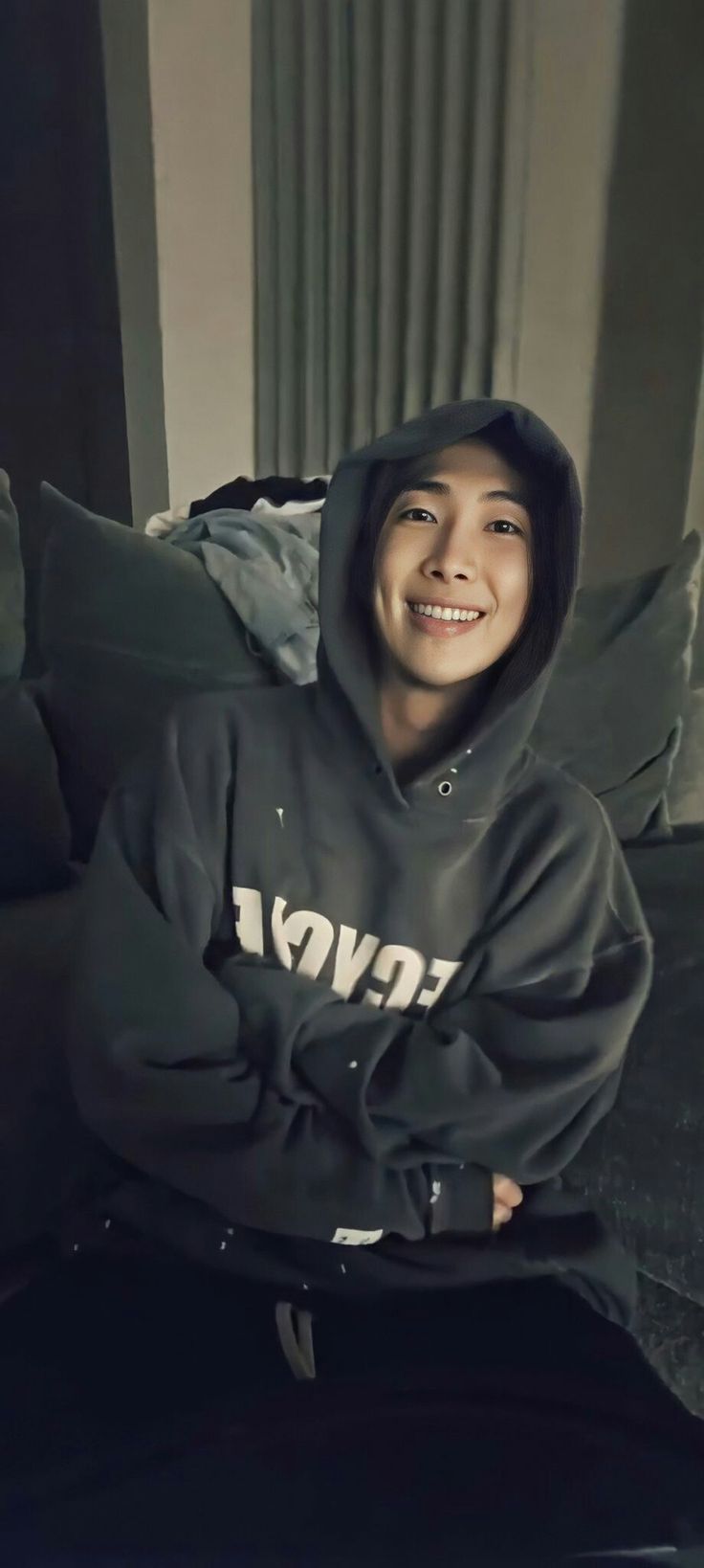 a person sitting on a couch wearing a black hoodie and smiling at the camera