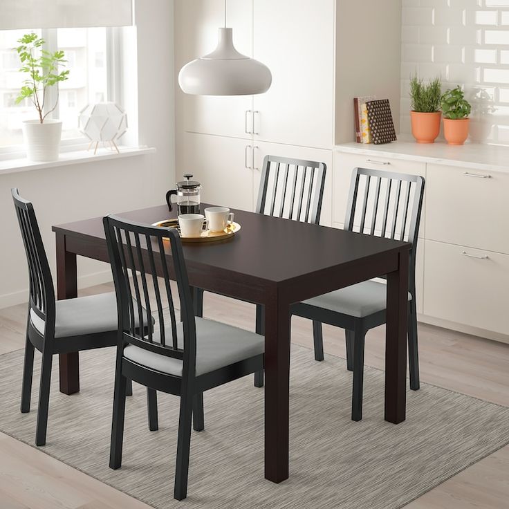 a dining room table with four chairs and a potted plant in the corner next to it