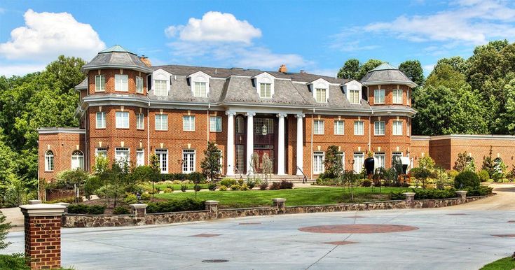 a large red brick house sitting in the middle of a lush green field with lots of trees