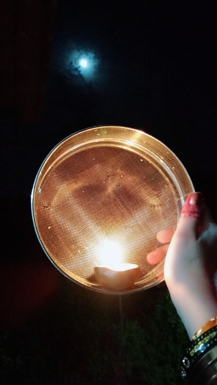 a person holding a lit candle in the dark with their hand on top of it