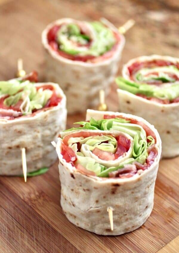 four wraps with meat, lettuce and tomato on them sitting on a cutting board