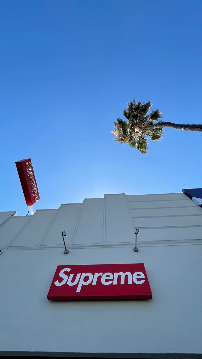 a red supreme sign on the side of a building with a palm tree in the background