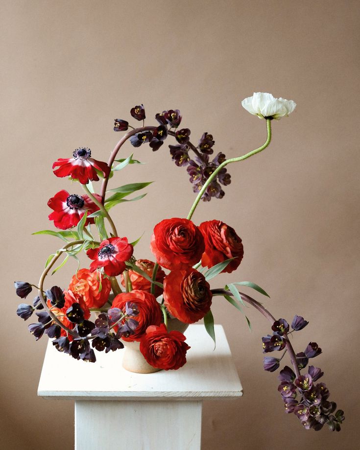 a vase filled with red and purple flowers on top of a white table next to a brown wall