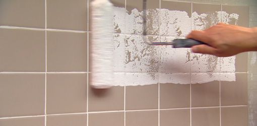 a person using a brush to paint a wall with white tiles on the bathroom walls