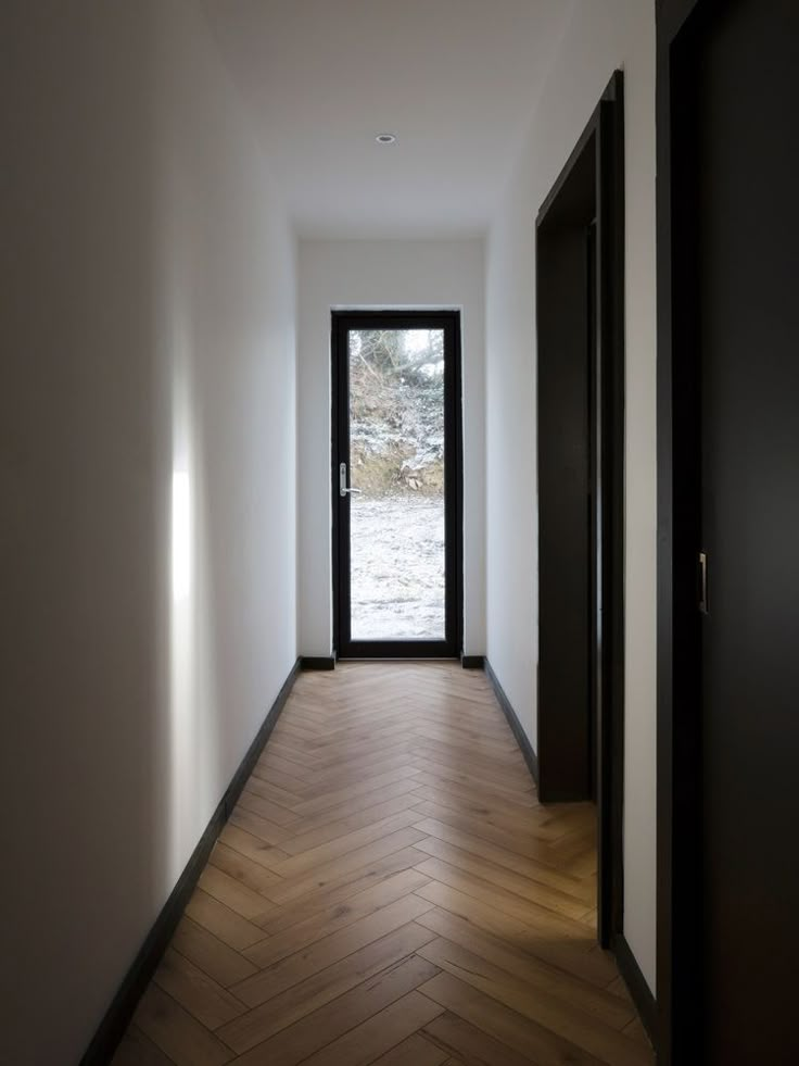 an empty hallway with wooden floors and black doors leading to another room that has white walls