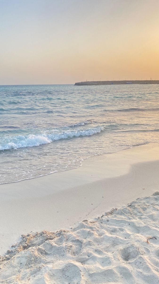 the surfboard is laying in the sand on the beach near the water's edge