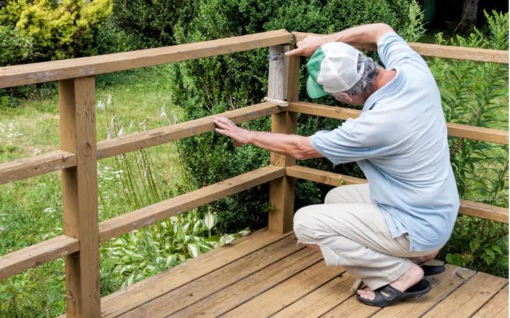 a man in blue shirt and khaki pants on wooden deck next to bushes