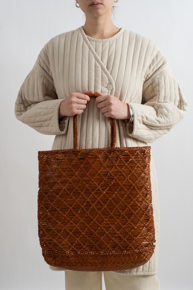 a woman is holding a brown woven bag