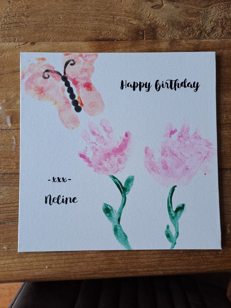 a birthday card with two pink flowers and a butterfly on the front, sitting on a wooden table