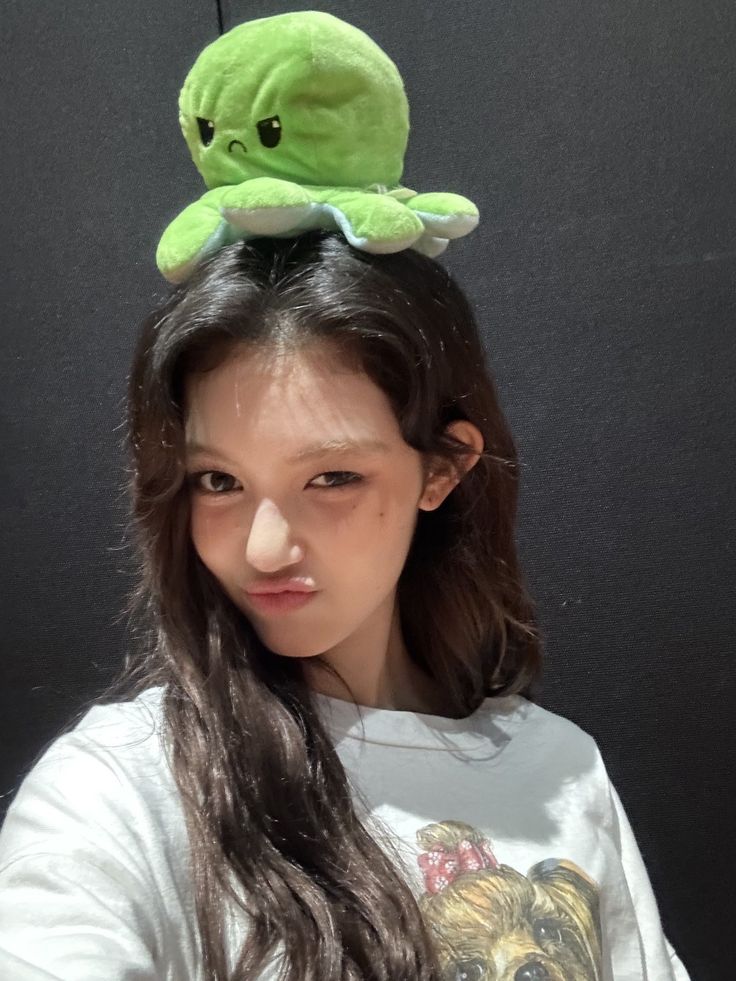 a girl with long hair and a green stuffed animal on her head