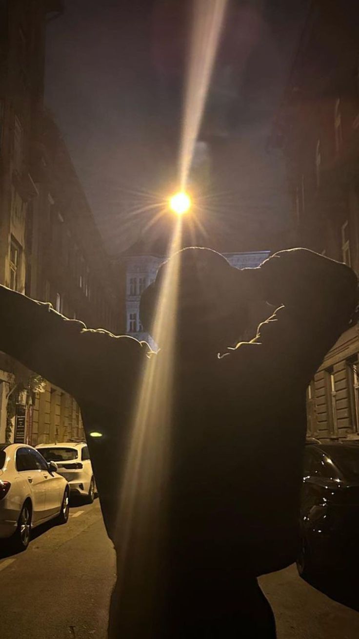 a person standing in the middle of a street at night with their arms stretched out